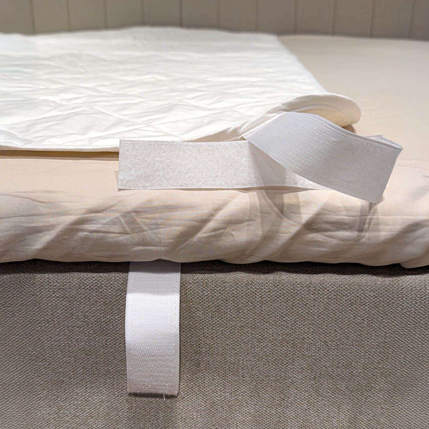 Canto do protetor de colchão branco e acolchoado dobrado para trás, deixando visível a tira de velcro à volta do rebordo da cama