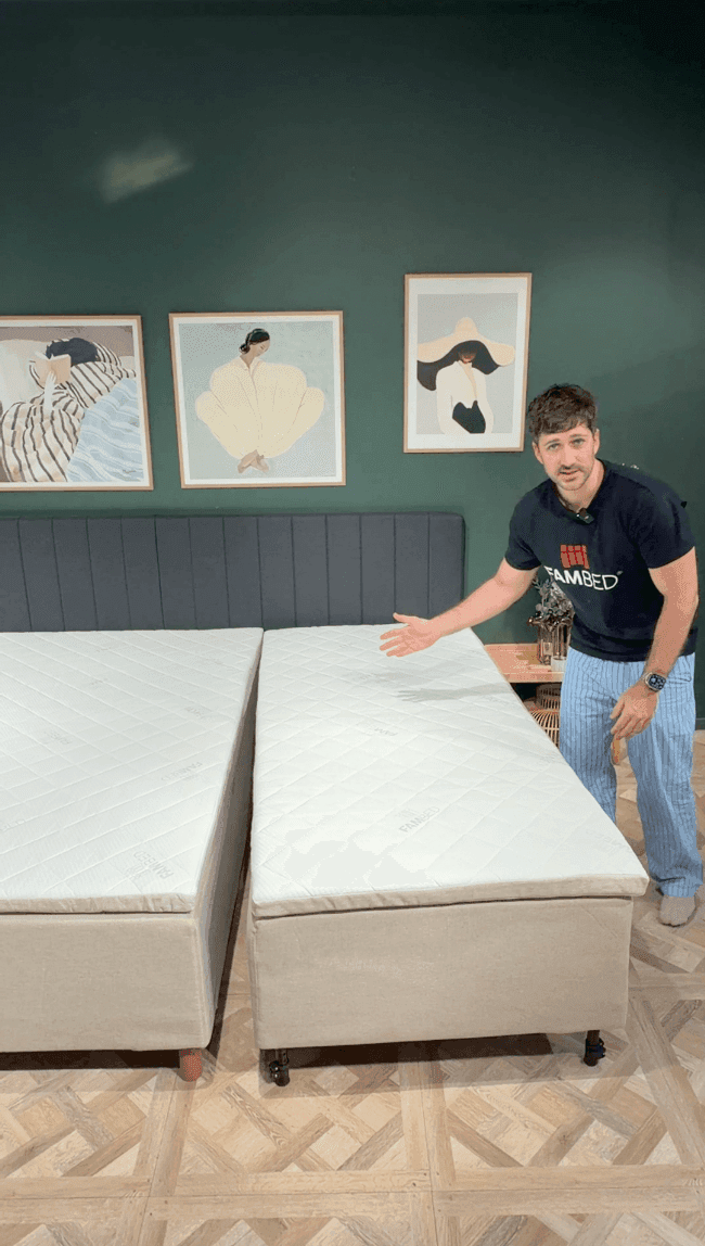 Um homem apresenta a cama de extensão com rodas, encostada à cama existente