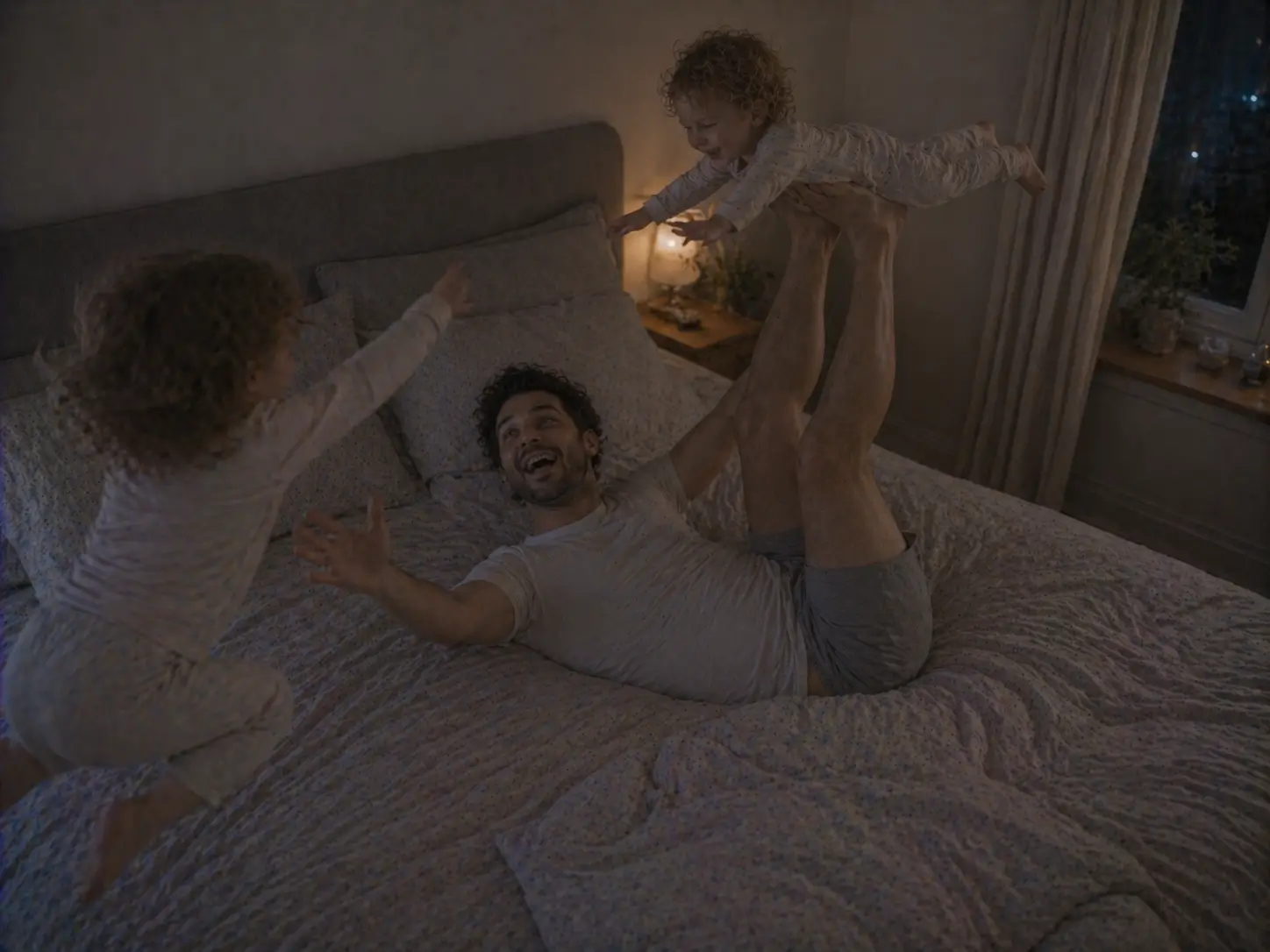Pai brinca aos aviões com uma das crianças na cama, enquanto a outra salta ao lado