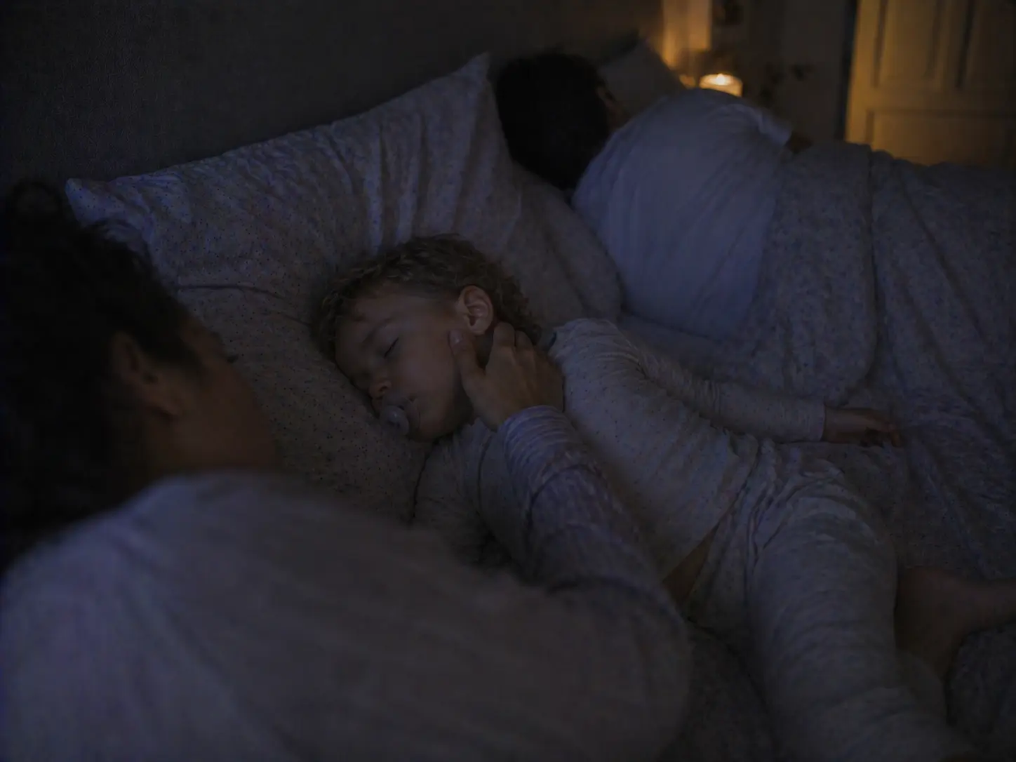 Mãe toca suavemente na face da criança adormecida na cama familiar durante a noite